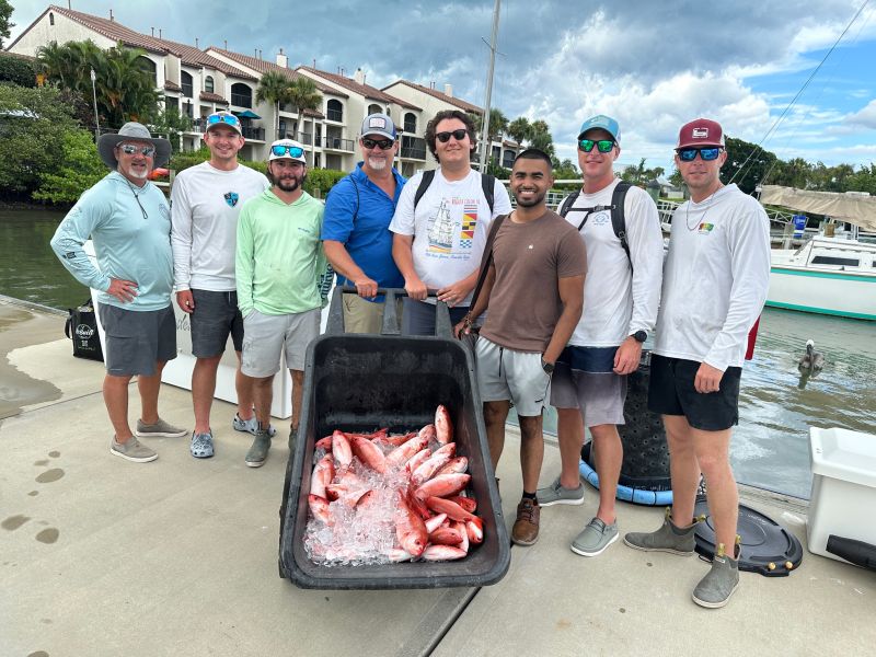 Group of men holding fish caught on a boat.