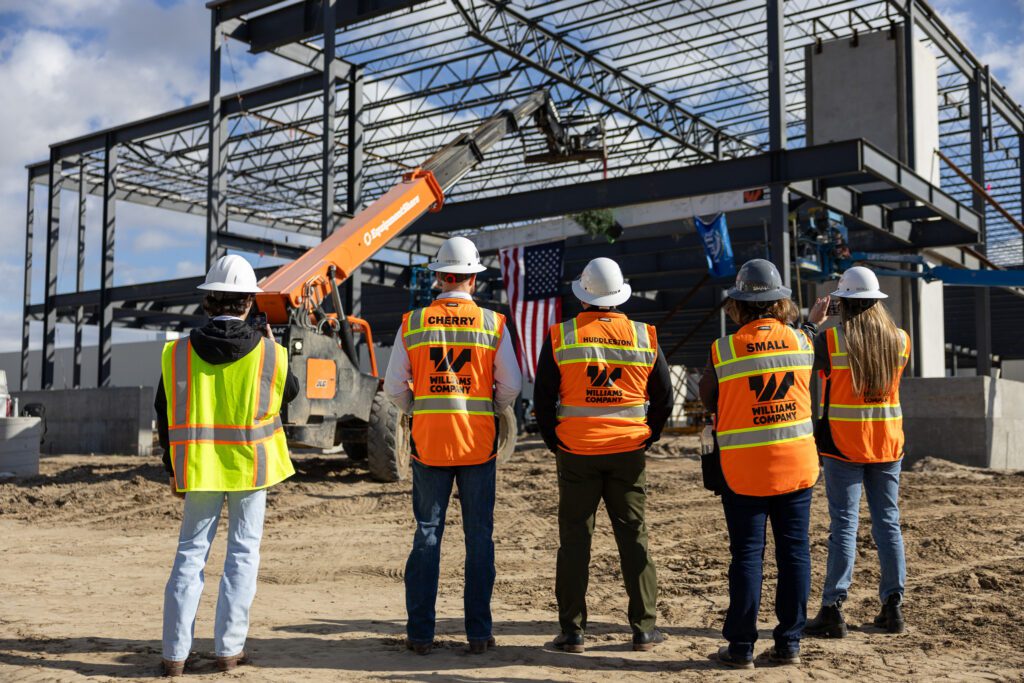 Four construction workers in safety gear observe a site with heavy machinery.