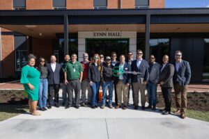 Group photo of diverse people outside Lynn Hall, some holding a trophy.