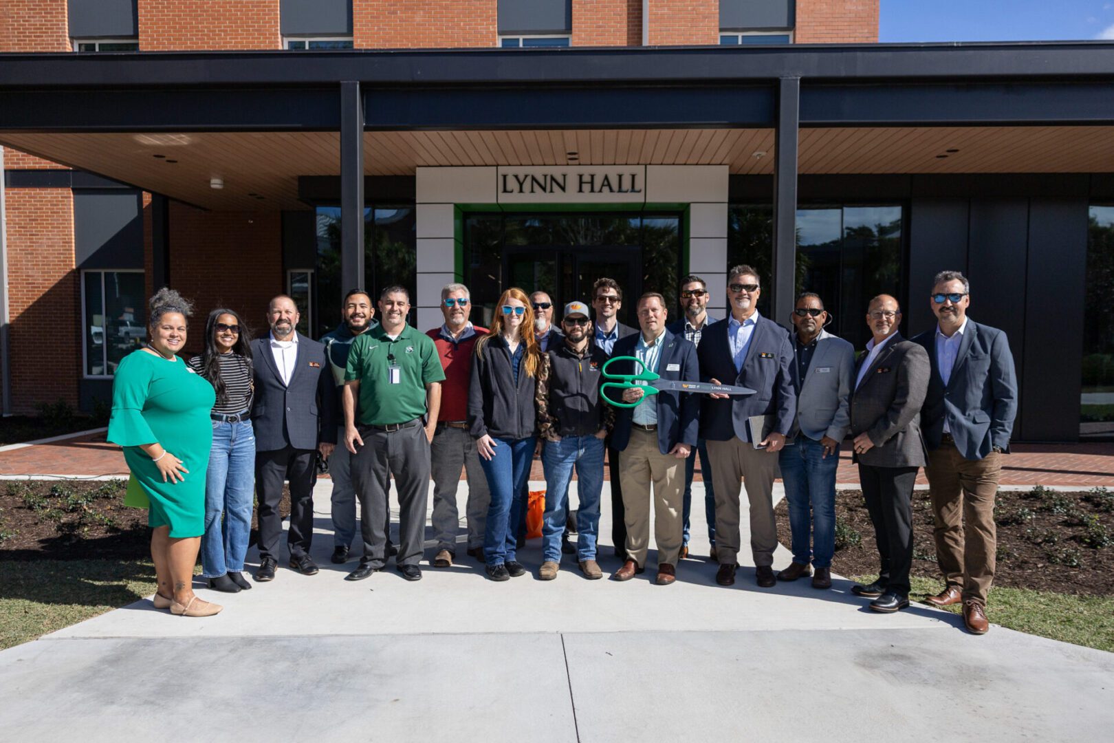 Group photo of diverse people outside Lynn Hall, some holding a trophy.