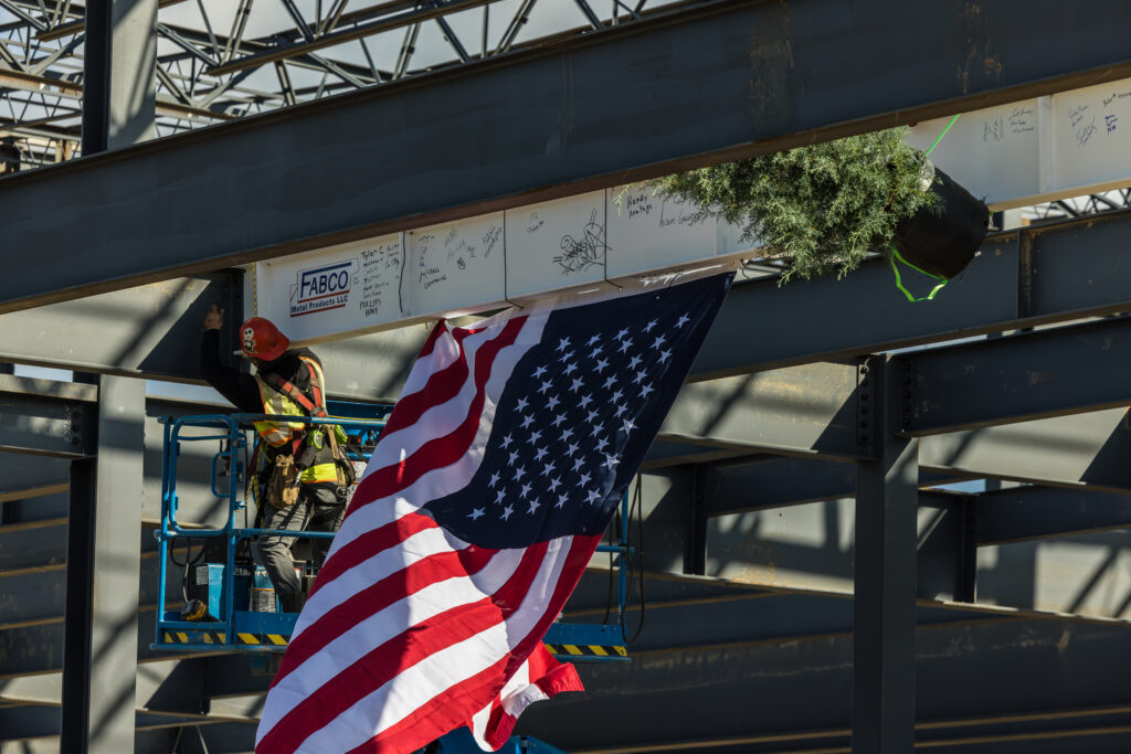Worker in safety gear near an American flag at a construction site.