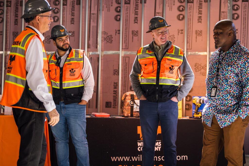 Two men wearing orange safety vests and hats standing in a construction site.
