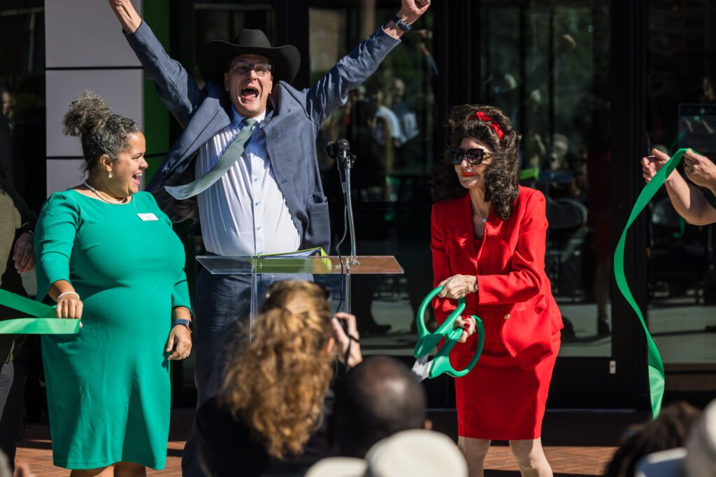 Three people celebrating outdoors, one holding a green ribbon.